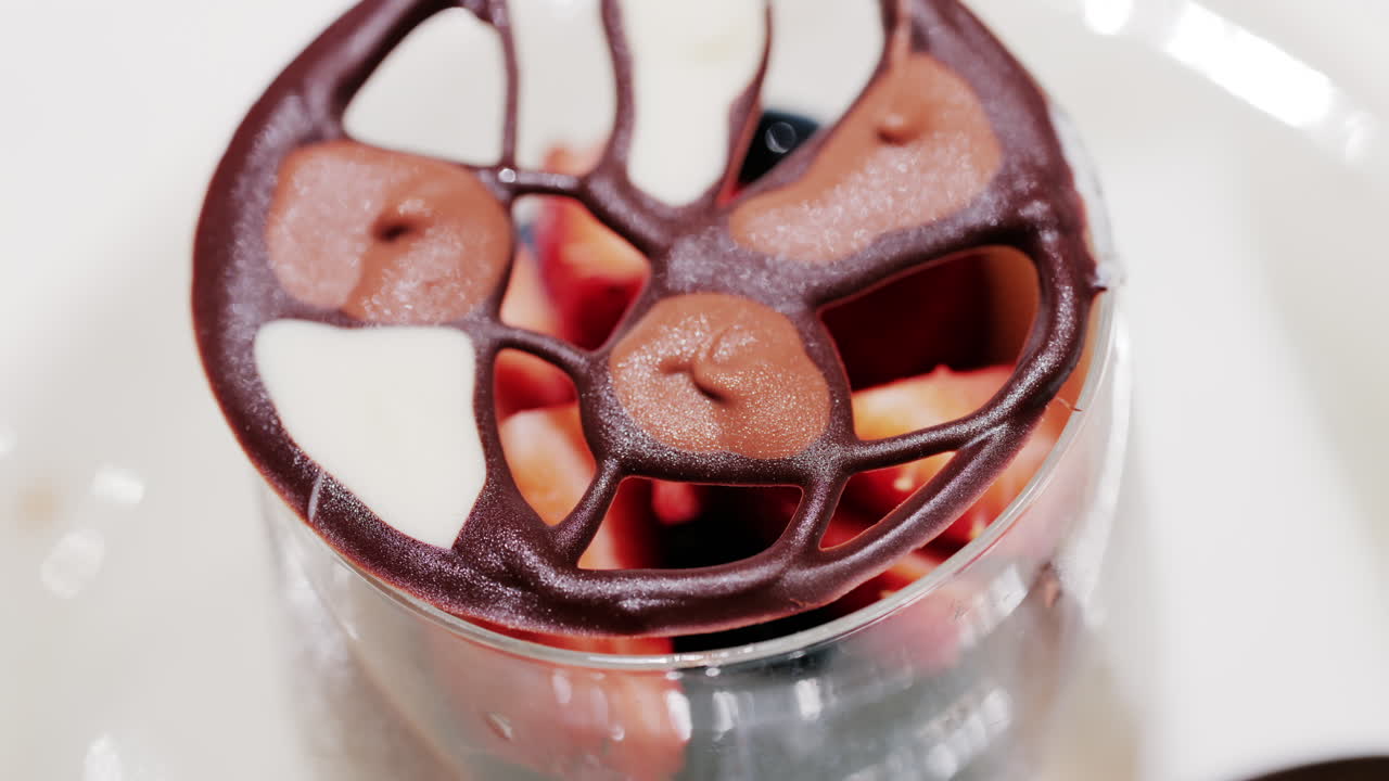 Elegant dessert in a glass topped with fresh strawberries, blueberries, and a chocolate lattice decoration