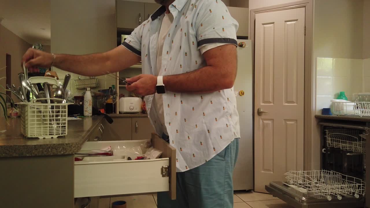 man putting the knives and forks and spoons back in the cutlery draw after putting it through the dishwasher, dishwasher open in the background