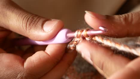 close-up of hands crocheting with pink crochet hook and brown yarn