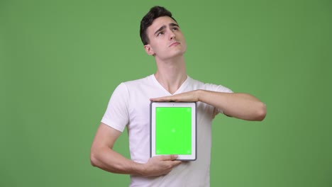 Young handsome man thinking while showing digital tablet