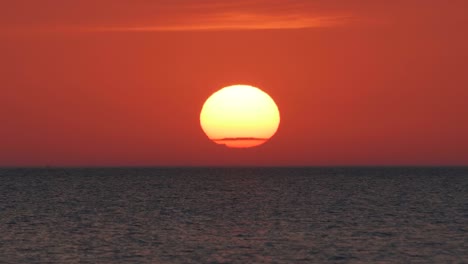 closeup sunrise over water, large red orange sun