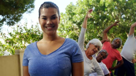 Trainer-smiling-at-camera-while-seniors-exercising-in-background-4k