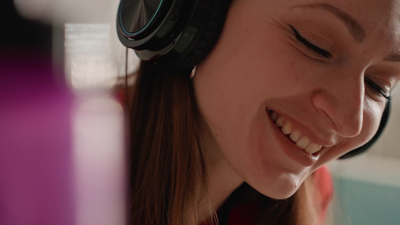 Donna bianca coach a casa con cuffie, ritratto ravvicinato con microfono e borraccia viola, sorridente e parlante mentre guida una sessione di fitness energica a casa, registrando audio motivazionale