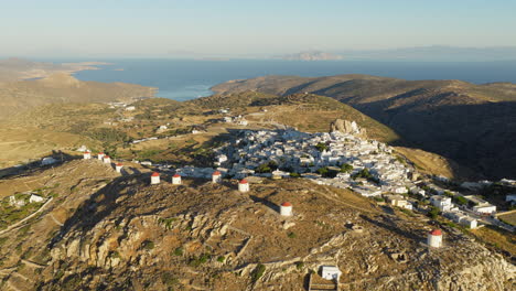 slow panoramic drone orbit of chora, amorgos at sunrise, showcasing the village’s iconic white windmills glowing in the soft morning light