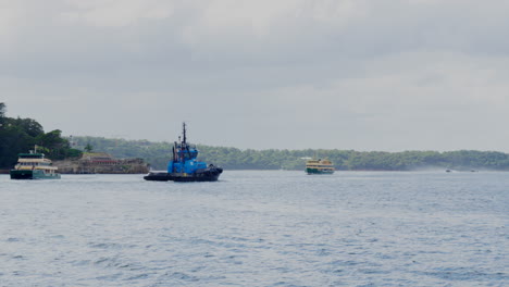 A-blue-tug-boat-crosses-Sydney-harbour-amongst-passenger-ferries,-in-Australia