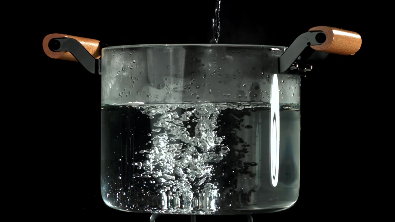 Acqua limpida che si versa in una pentola di vetro trasparente con bolle