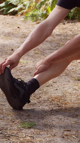 vertical video close up of man warming up and stretching legs and feet before work out exercising running through forest shot in real time