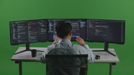 back view of asian man developer having headache while write code with multiple computer screens in green screen studio