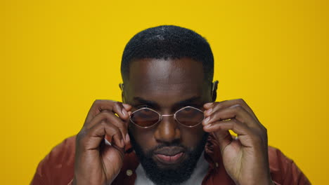 portrait of serious african man putting sunglasses in yellow background.