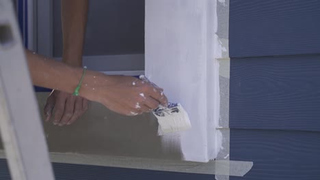 slow motion shot of person painting window frame with brush on wooden house outdoors - renovation of house facade