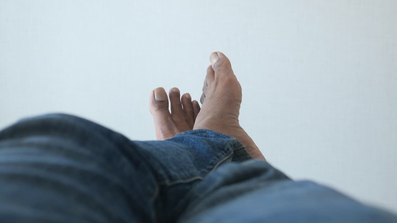 Close up of a man's feet in blue jeans resting on a white surface