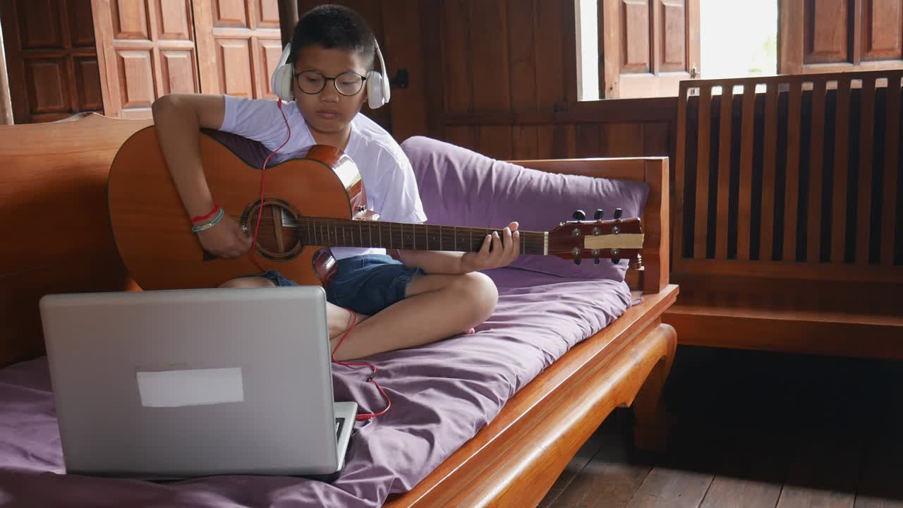 A boy plays guitar online at his home.