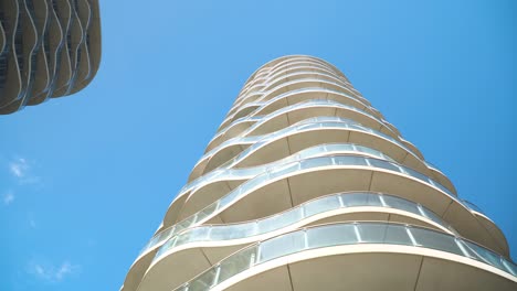 tall modern buildings all white glass balcony wavy futuristic looking unusual design luxury architecture holiday resort bottom looking up view moving wide shot sign post over the frame clear blue sky