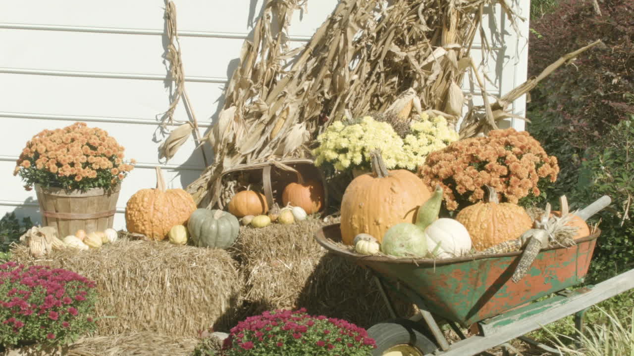 Autumn harvest decorations in front of a white house on a sunny fall day.  Pumpkins, squash, corn.