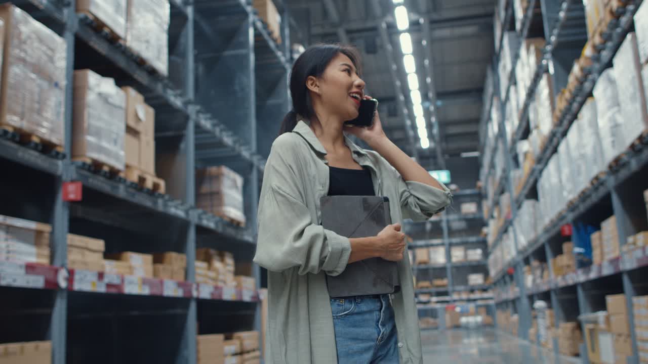 Giovane imprenditrice asiatica venditrice online che parla confermando ordini dal cliente al telefono, tenendo un tablet digitale e in piedi in un centro commerciale.