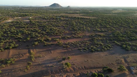 establishing drone shot moving forward towards mountain peak surrounded by rich green vegetation and brown - orange soil at morning sunrise