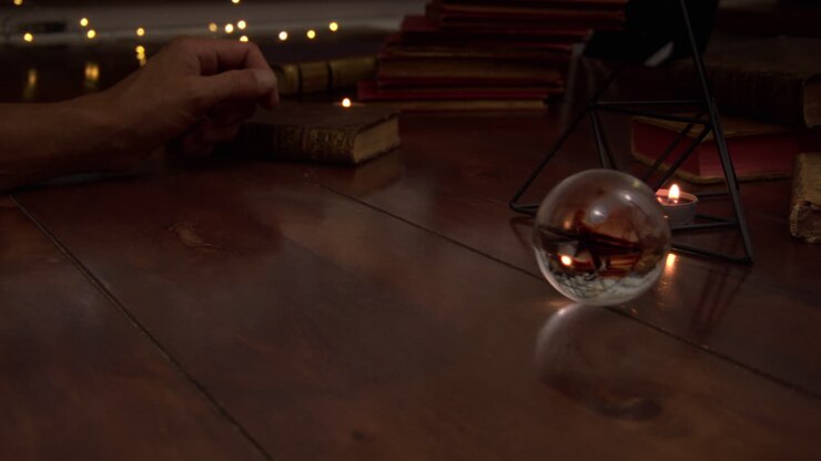 Several candles are lit on the table, antique books, iron pyramid and antique books are visible