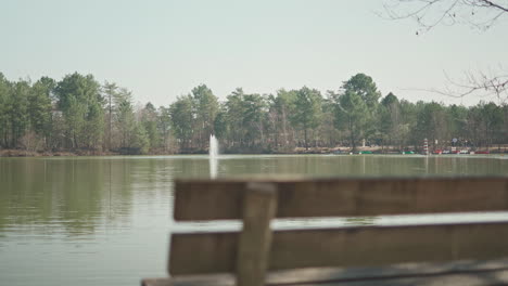 focus pull to the left side of a wooden bench in front of a lake with a water fountain in the middle