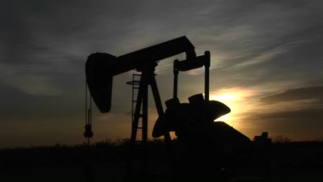 medium shot of a silhouetted oil pump turning in the new mexico desert