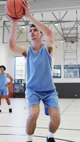 vertical video of diverse male basketball team training in indoor court, in slow motion