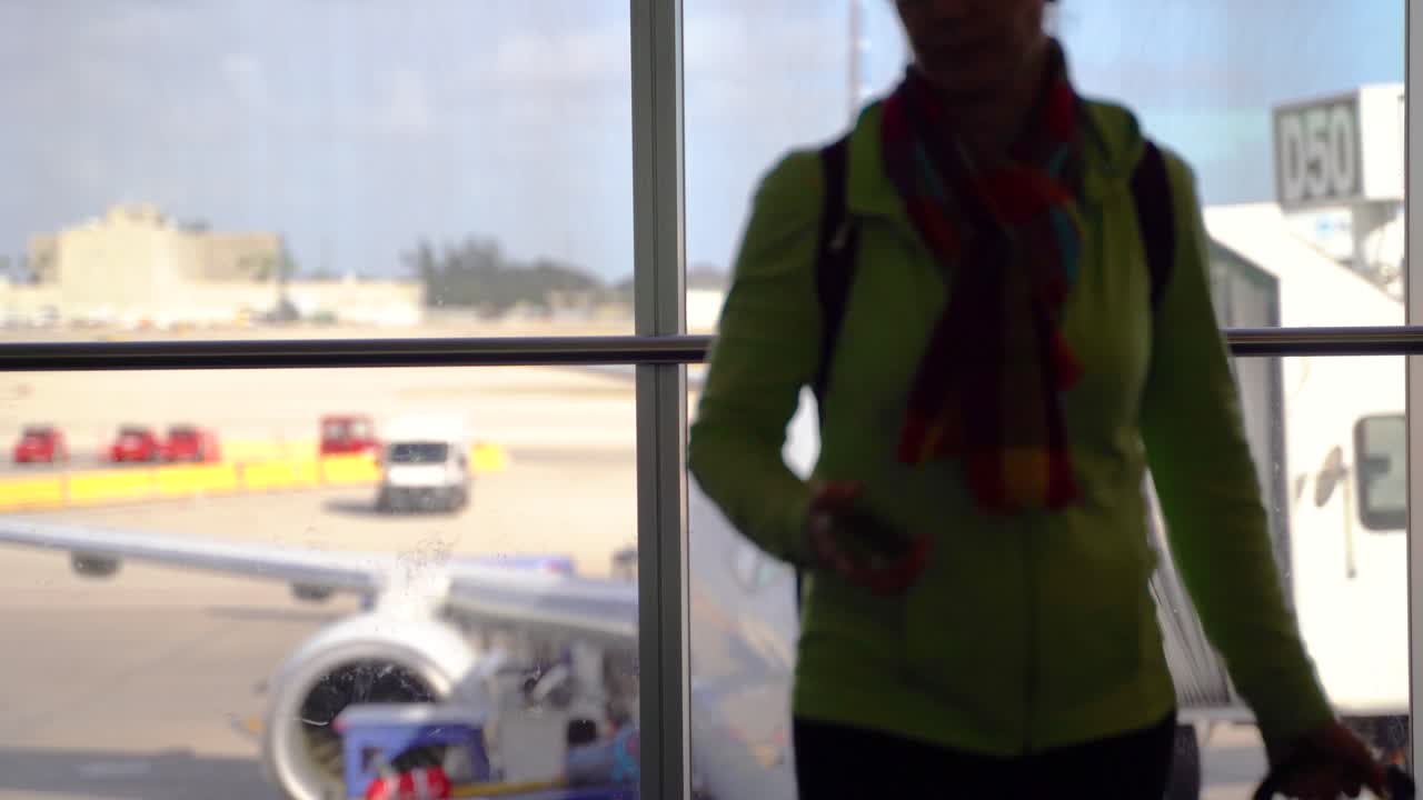 silueta de mujer guardando su teléfono y saliendo del marco con un avión borroso a distancia en la puerta de embarque