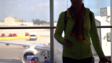 silhouette of woman putting her phone away and rolling out of the frame with blurry airplane in distance at the boarding gate