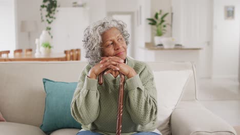 Portrait-of-happy-senior-african-american-woman-sitting-on-sofa,-leaning-on-walking-cane