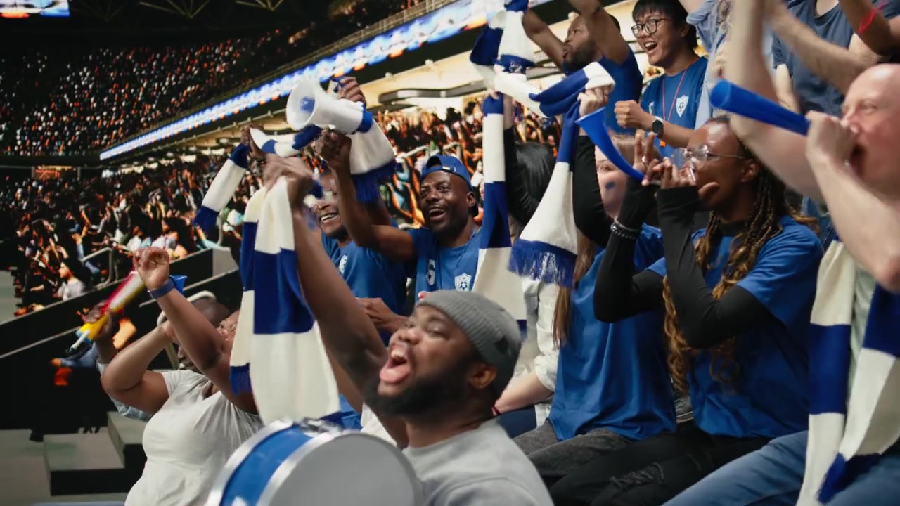 Aficionados de fútbol del equipo azul animando en una sección de aficionados abarrotada del estadio