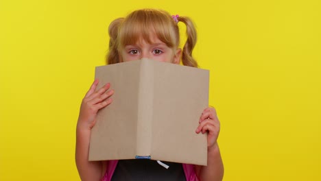 Funny-kid-primary-school-girl-with-ponytails-wearing-uniform-peeping-while-hiding-behind-a-book