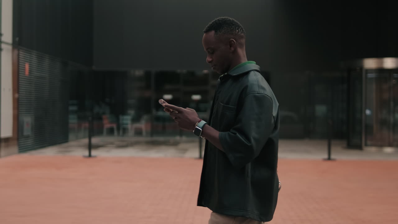 Young Black Man Walking and Using Smartphone Outdoors