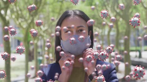 animation of covid 19 cells over woman in park wearing face mask