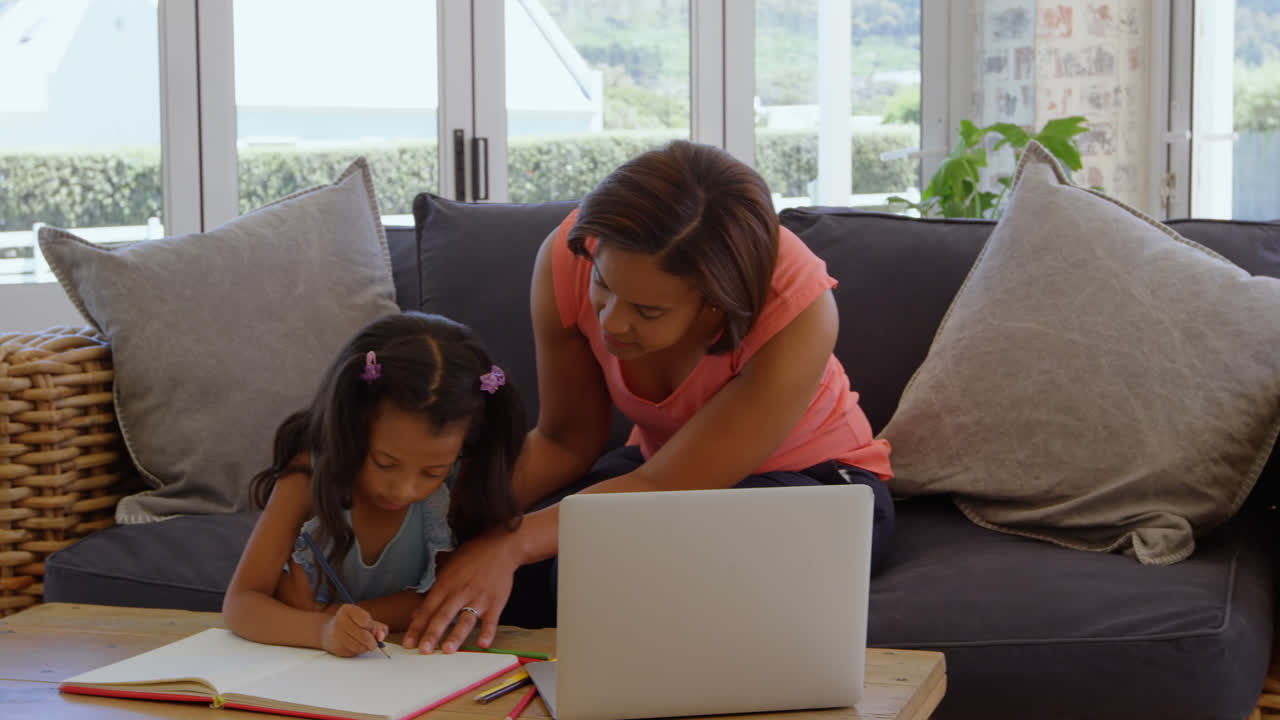 Vista frontal de madre afroamericana madura ayudando a su hija con la tarea en un hogar cómodo 4k