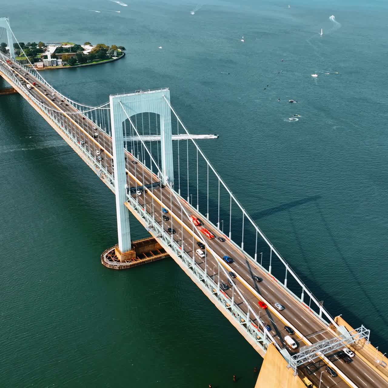 Cars running quickly by the long suspension bridge on sunny day. Top view of the Throgs Neck Bridge and the East river with boats on
