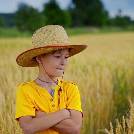 boy in straw hat outdoors. portrait of a little farmer on yellow field background. cheerful kid stands among agricultural plants.
