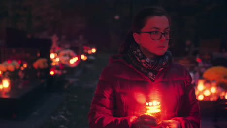 mujer caminando por el cementerio por la noche sosteniendo una vela encendida