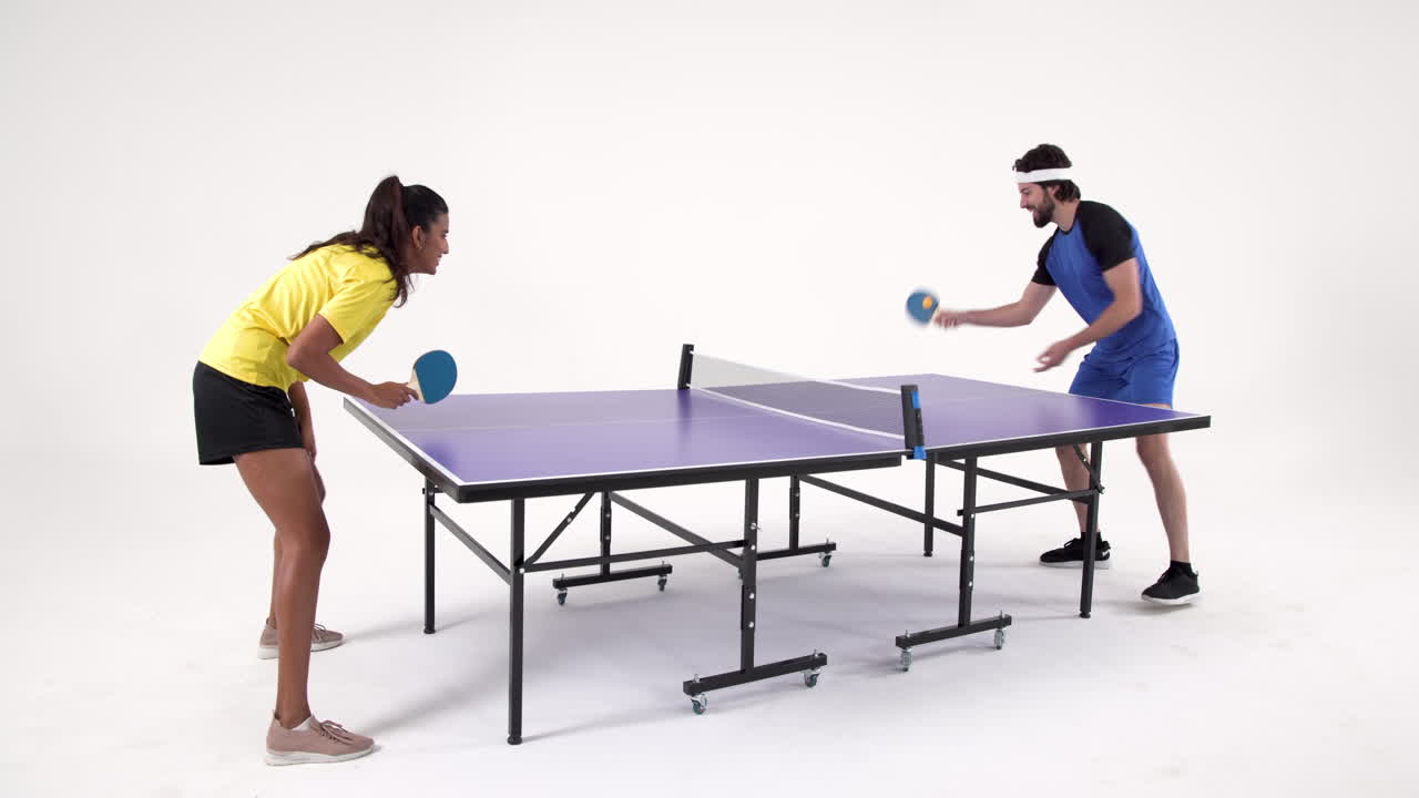 Playing table tennis, man and woman enjoying game in studio setting