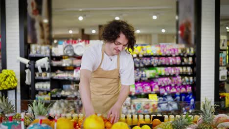 Un-Chico-Feliz-Con-Cabello-Castaño-Rizado,-Trabajador-De-Supermercado,-Coloca-Frutas-En-El-Estante-Durante-Su-Trabajo-En-El-Supermercado.