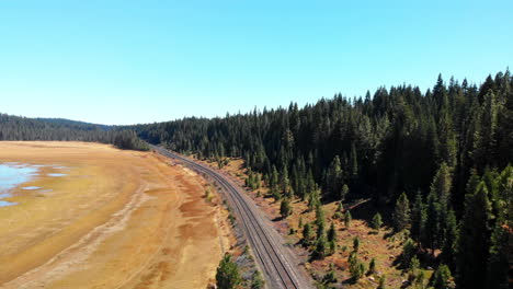 Vuelo-Aéreo-Sobre-Ferrocarriles-De-Montaña-Que-Vuelan-Sobre-Un-Lago-Seco,-Ahora-Un-Campo-De-Hierba