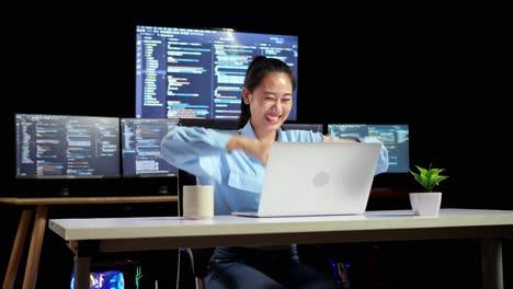 asian female programmer celebrating succeed writing code by a laptop using multiple monitors showing database on terminal window desktops in the office