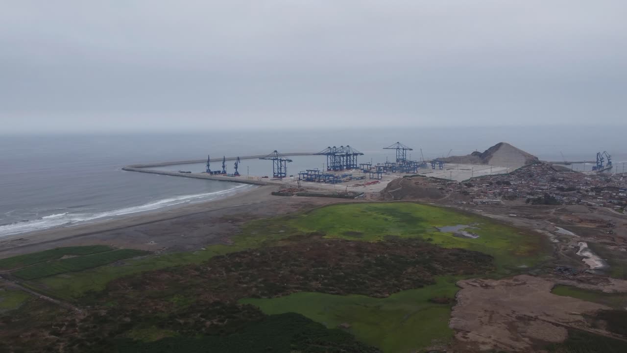 Aerial shot of a construction site of megaport being built in Peru in the city of Chancay. Drone flies above wetlands towards the port. Big blue cranes can be seen in the distance.