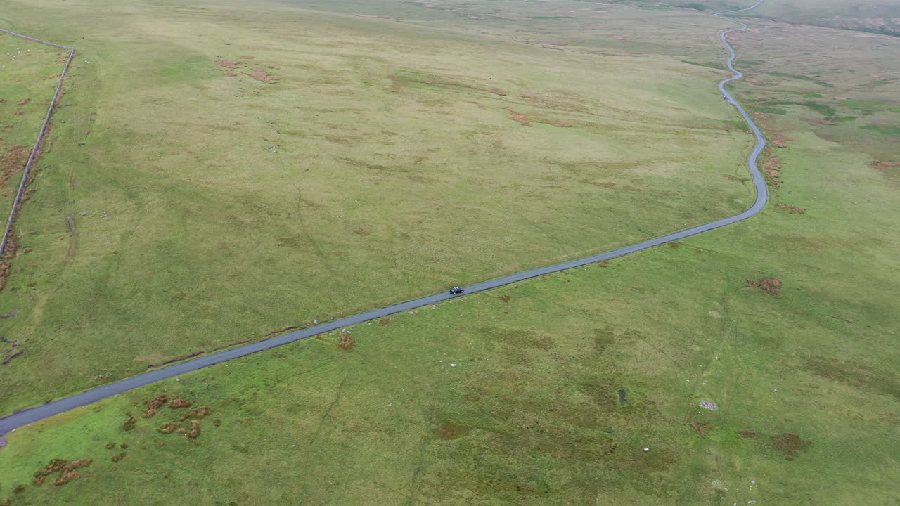 toma aérea de un coche negro conduciendo por una carretera rural en el distrito inglés de los lagos, día soleado