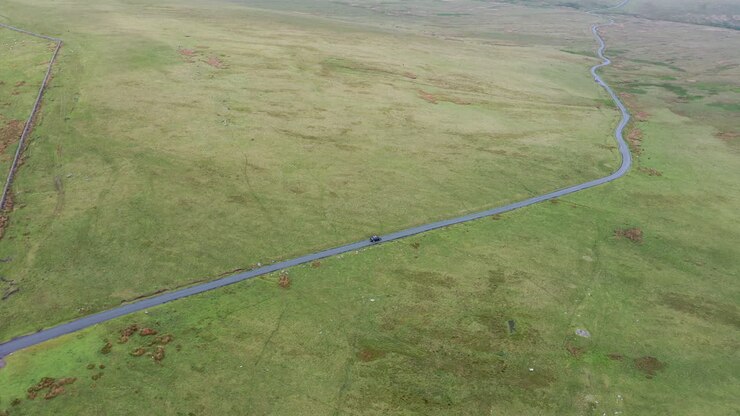 Aerial follow shot of a black car driving on a country road in the English Lake District, bright sunny day
