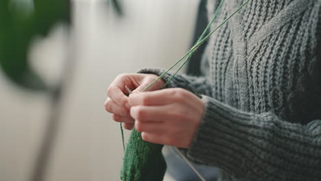 the hands of an unrecognizable woman knitting with green wool 1