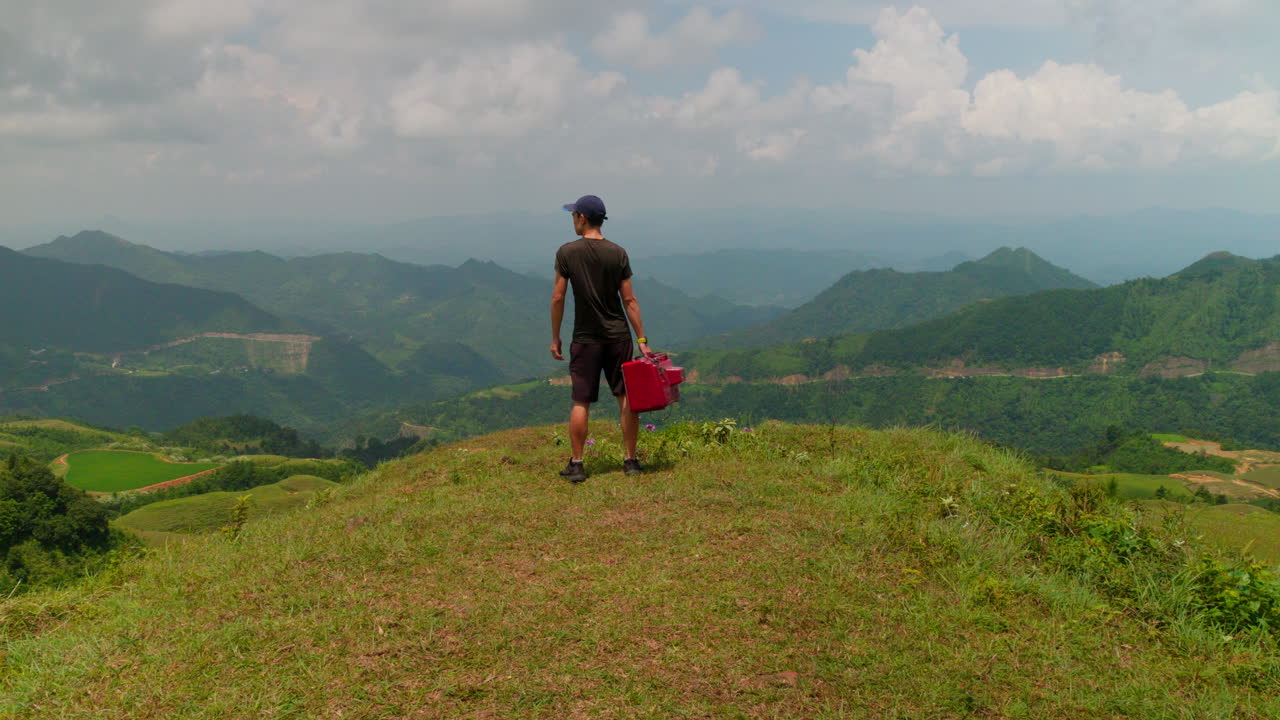 산의 풍경을 보는 동안 빨간색 오래된 tv를 들고 있는 남성의 이상한 비디오
