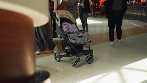 a busy mall scene with different people wearing various clothes in the background. a baby stroller is prominently featured, adding to the dynamic environment