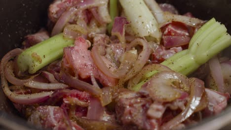 remuer le jarret de boeuf mélangé avec des tranches d'oignon, du céleri et des épices avec une cuillère en bois à l'intérieur d'une marmite profonde