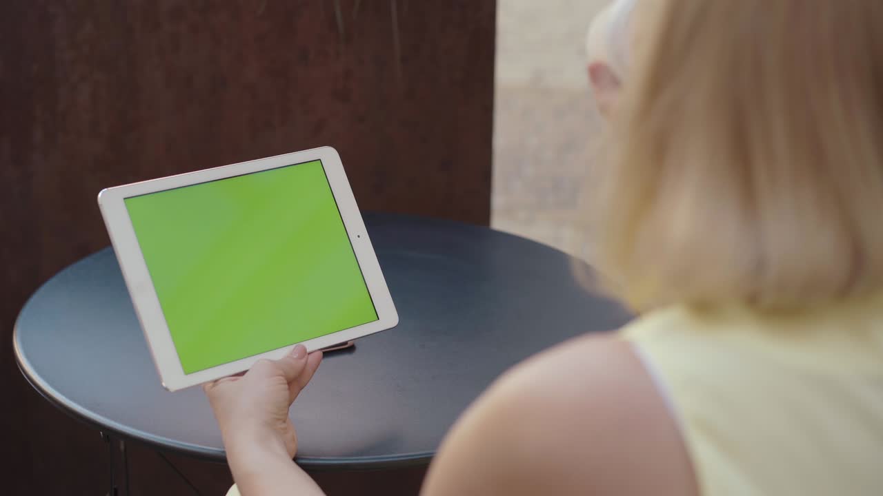 una mujer irreconocible sosteniendo una tableta con pantalla chromakey al aire libre y bebiendo café. una mujer rubia caucásica de mediana edad viendo algo en línea. comunicación inalámbrica, navegando por internet.