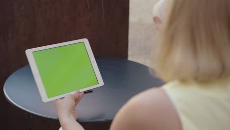 una mujer irreconocible sosteniendo una tableta con pantalla chromakey al aire libre y bebiendo café. una mujer rubia caucásica de mediana edad viendo algo en línea. comunicación inalámbrica, navegando por internet.