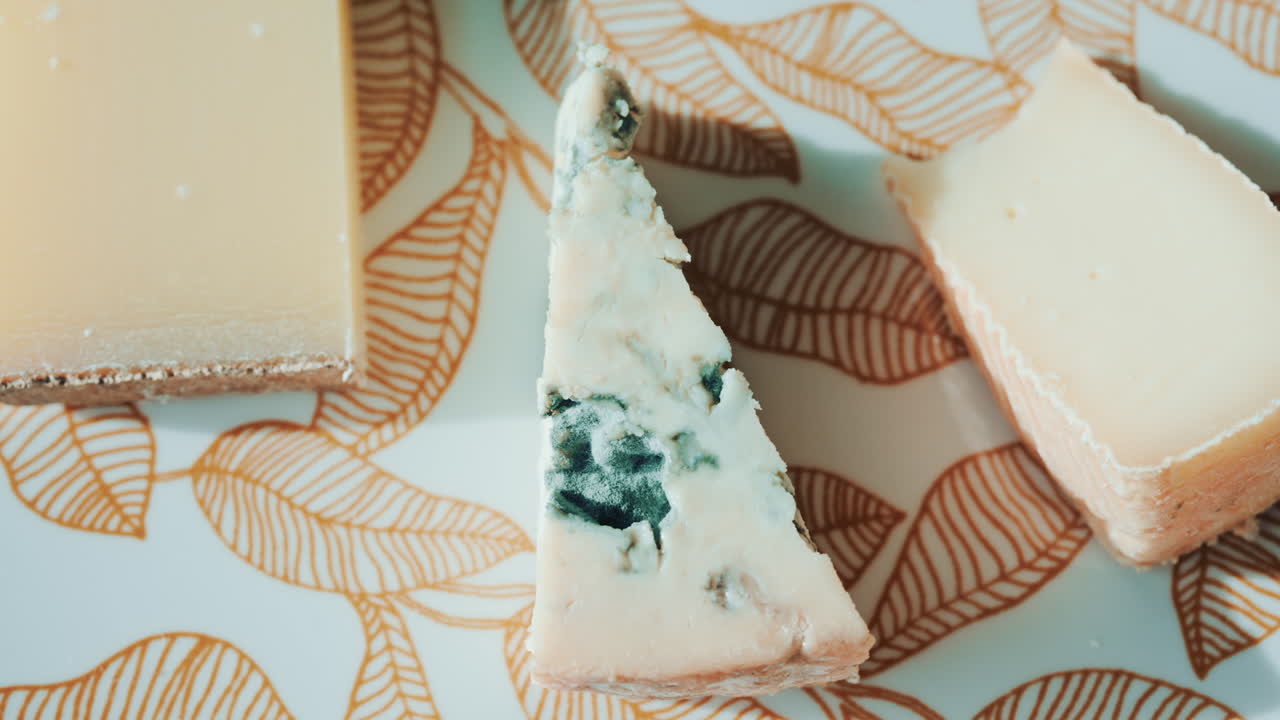 Close up of a cheese plate with assorted cheeses and salad on an elegant patterned plate