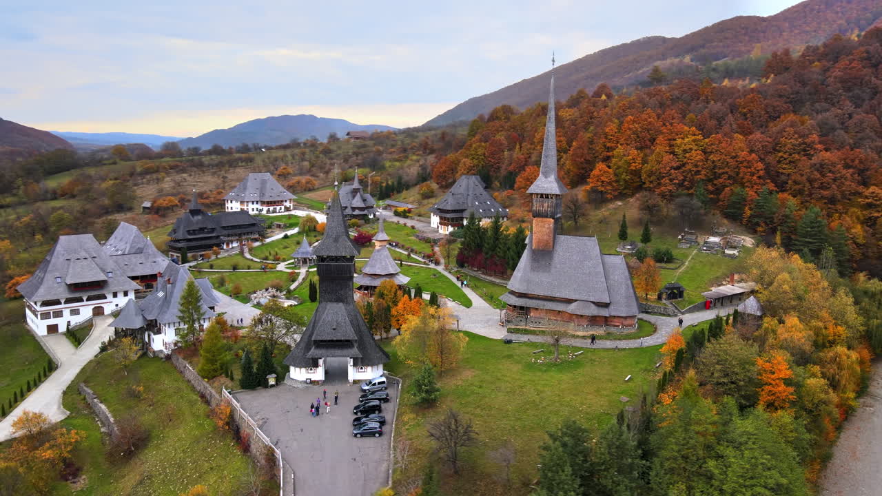 Aerial drone view of the Barsana Monastery, Romania. Main church and other buildings, visitors, hills covered with yellowing forest around
